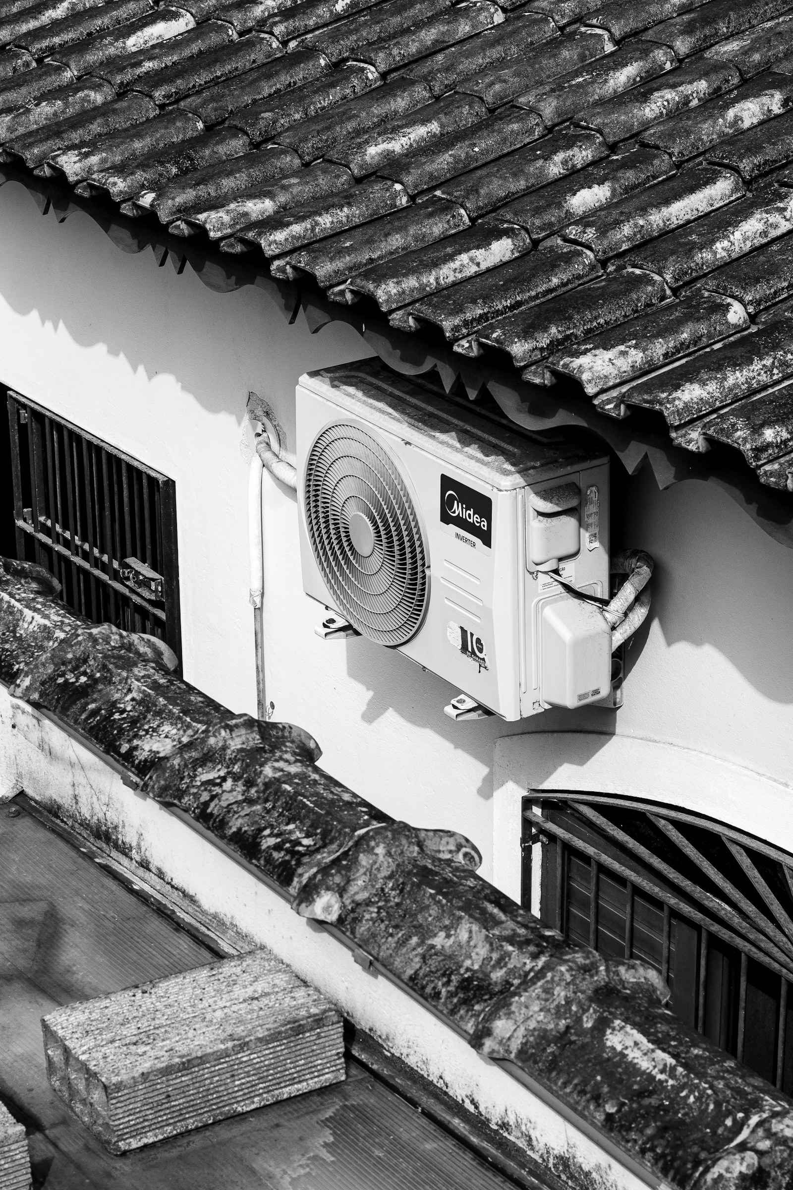 An exterior wall-mounted air-conditioning unit under a tiled eave