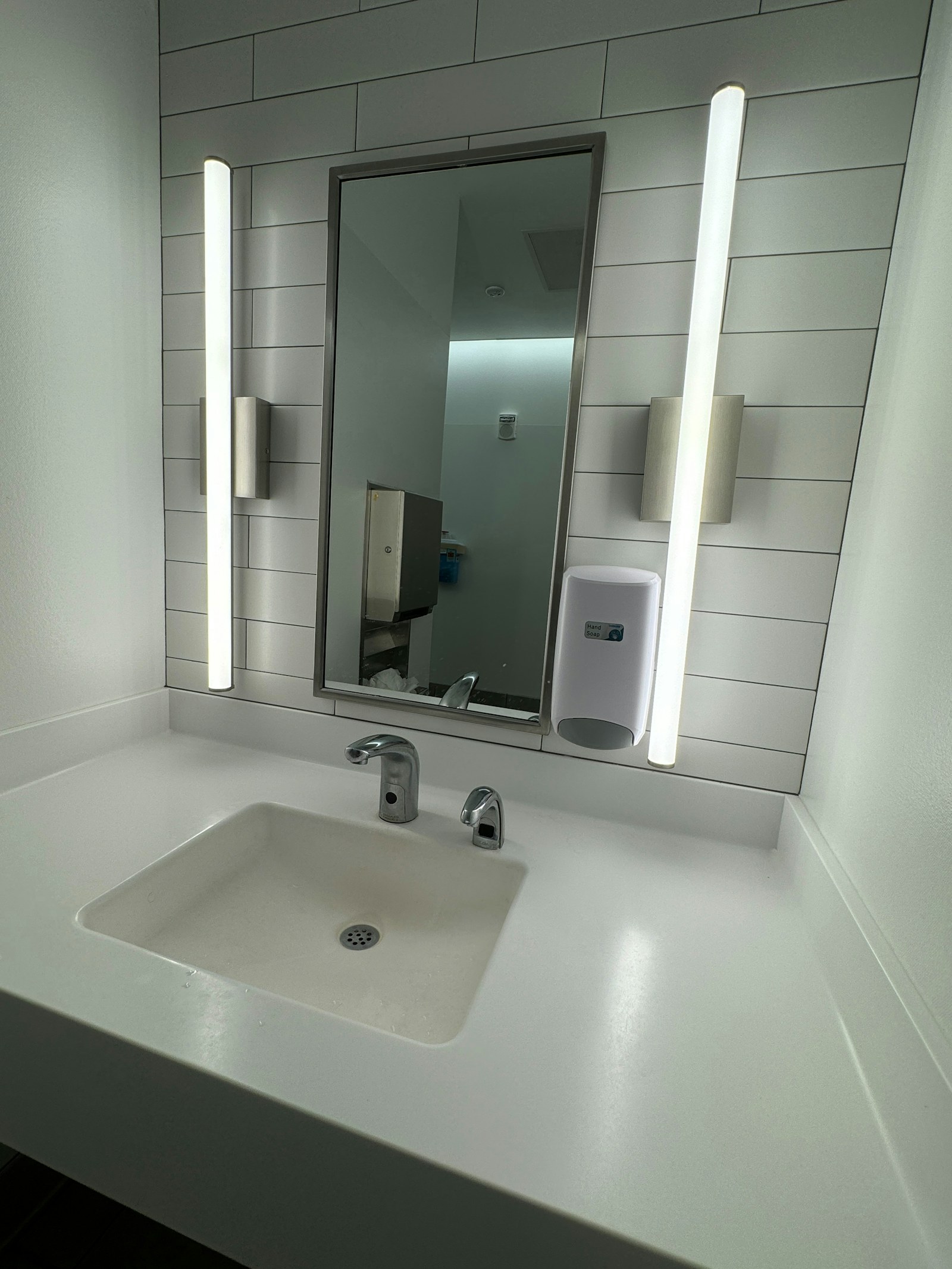 A bathroom sink, mirror and soap dispenser in a clean vanity area