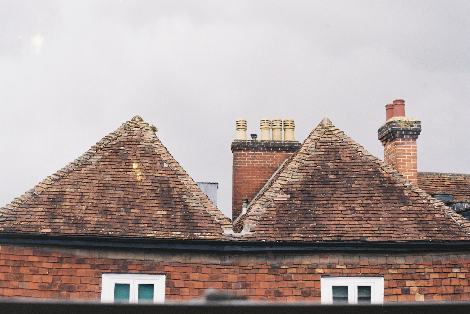 Finished tiled rooftops and brick chimneys against the sky; full roof replacement and new roof installation.